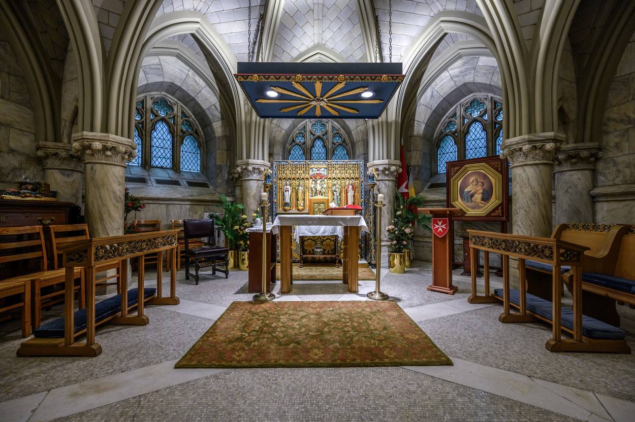 The Sacristy Chapel: a gilded reredos with the Crucifixion at its center, beneath plain blue leaded-quarry windows set in the vaulted marble chapel.