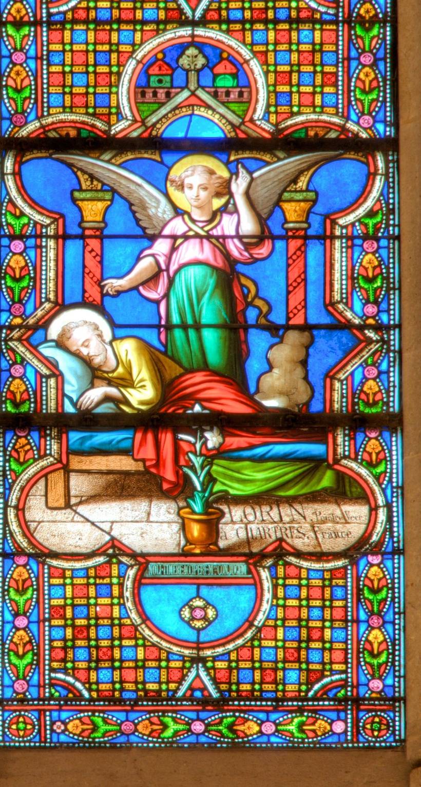 Joseph's Dream: an angel stands over the sleeping Joseph, with a lily in a pot at the foot of the bed and the glazier's signature painted along the stone sill.