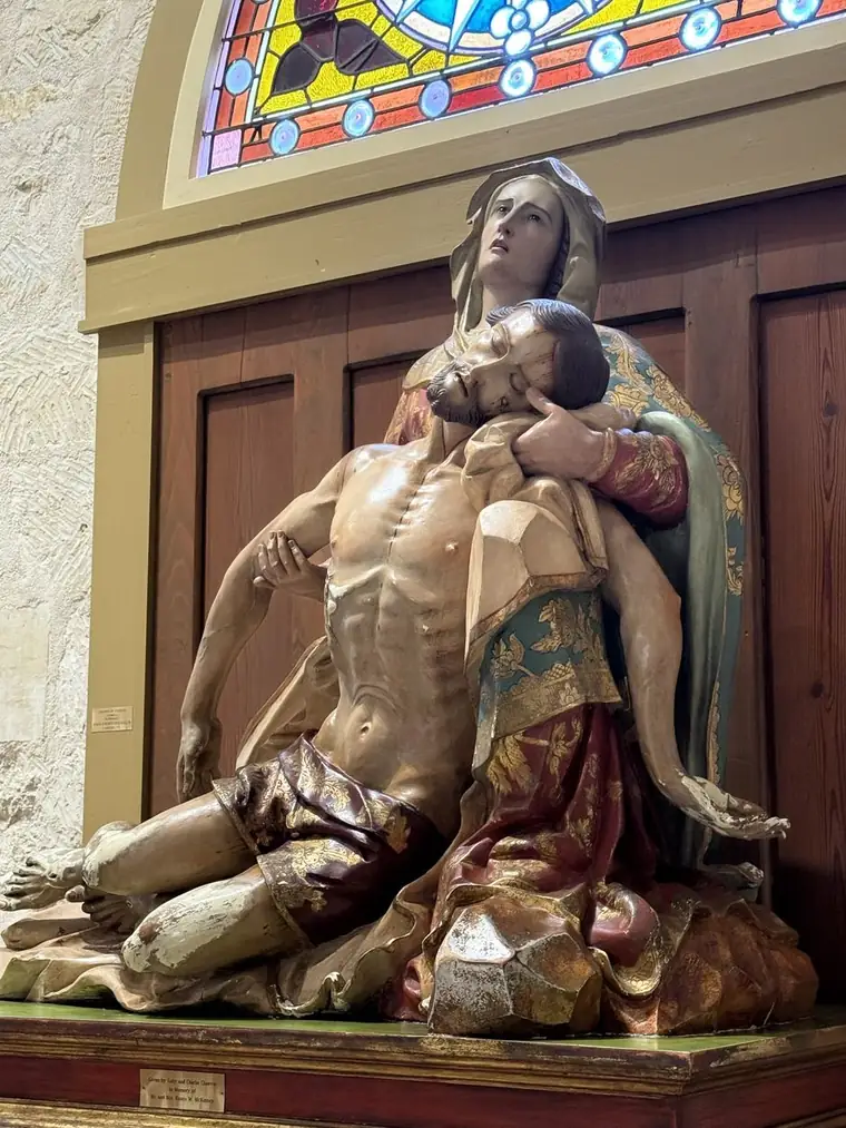A polychrome Pietà: the Virgin looking upward with the body of Christ across her lap, beneath a stained glass lancet.
