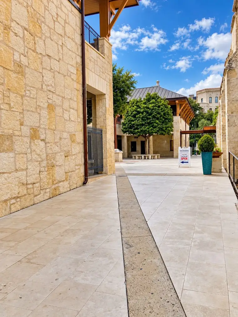 The paved walkway leading into Plaza de la Cruz between limestone buildings, with the bookstore's open sign and its blue arrow pointing the way.